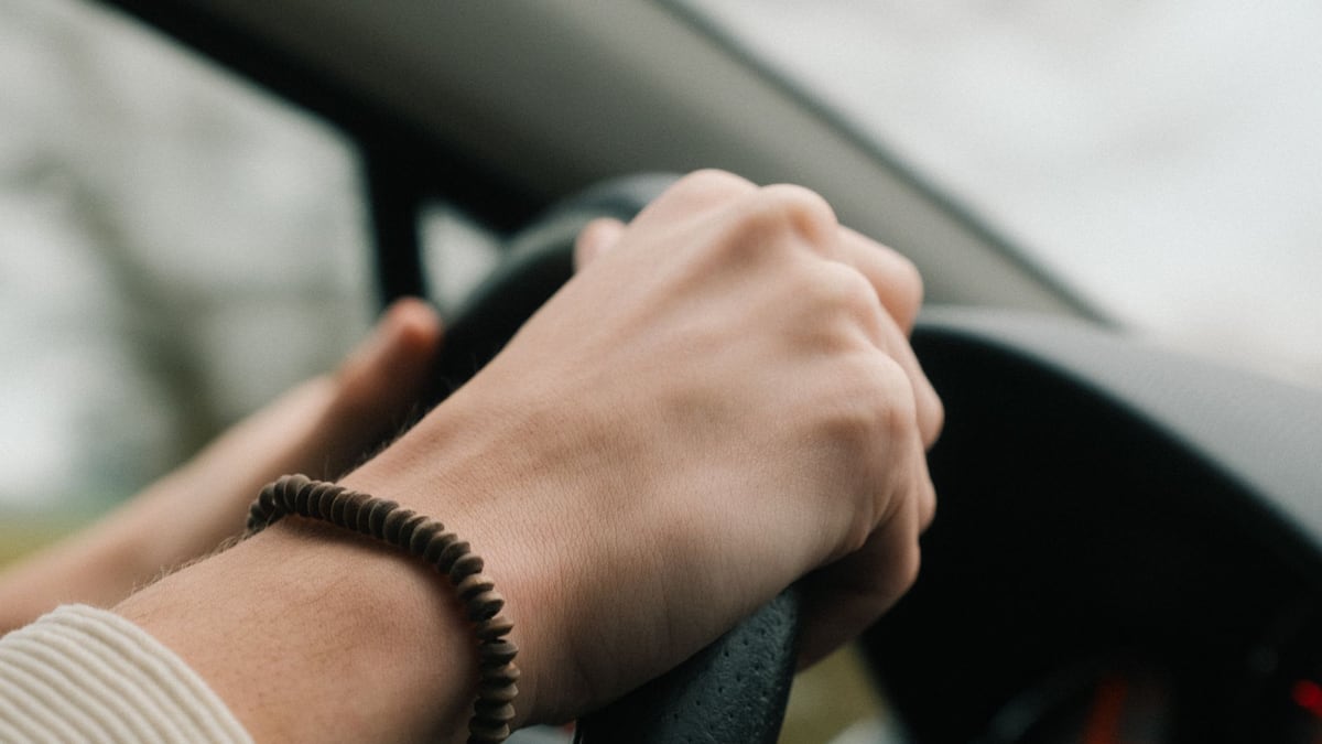 Detail of hands holding car steering wheel, wearing bracelet, while driving