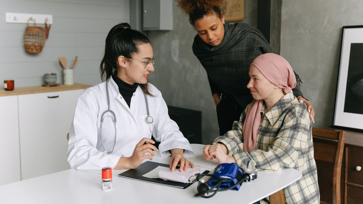 A doctor consulting with cancer patient and friend at home, offering support.
